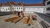 Einige Jugendliche und Erwachsene stehen auf einer Dachterrasse, auf der sich einige Stapel Holzpfosten und Bretter sowie eine aus Pfosten und Brettern zusammengebaute Konstruktion befinden. Im Hintergrund sind einige Altbauten sowie rechts ein neues Gebäude zu sehen.